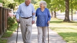 Senior couple walking arm-in-arm on a sunny sidewalk, each using a cane.